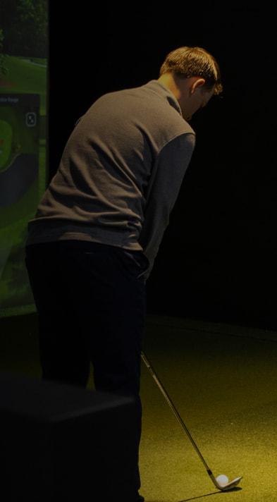 Person playing indoor golf, focusing on putting a golf ball on a green surface, with a dark background.