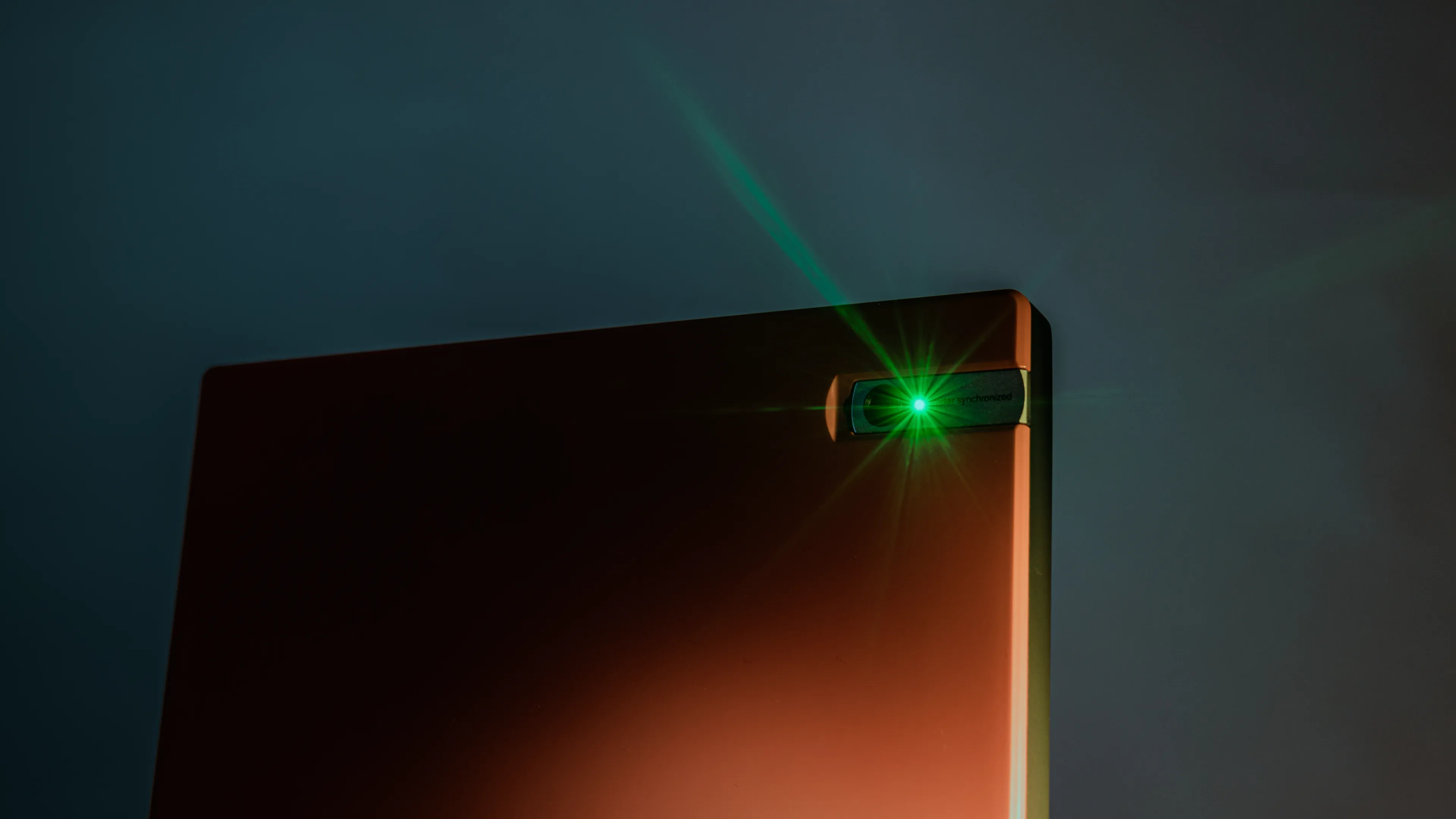 Close-up of a sleek electronic device corner with a glowing green LED light, set against a gradient blue and orange background.