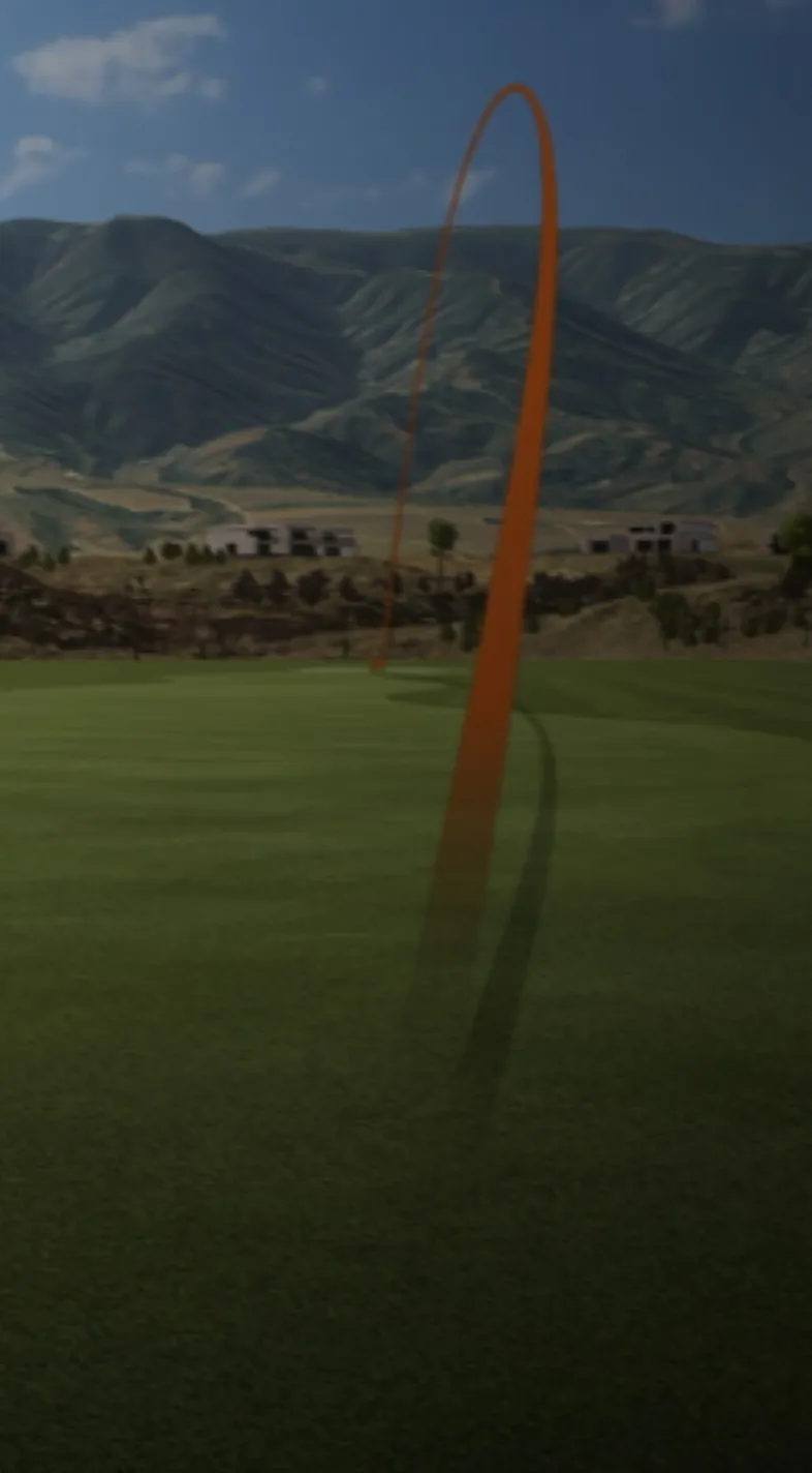 A golf ball's trajectory is traced by an orange arc over a green fairway, with distant mountains under a clear blue sky.